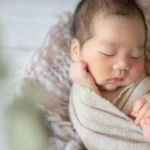 ニューボーンフォト_ニュートラルカラーの布に包まれて眠る赤ちゃん