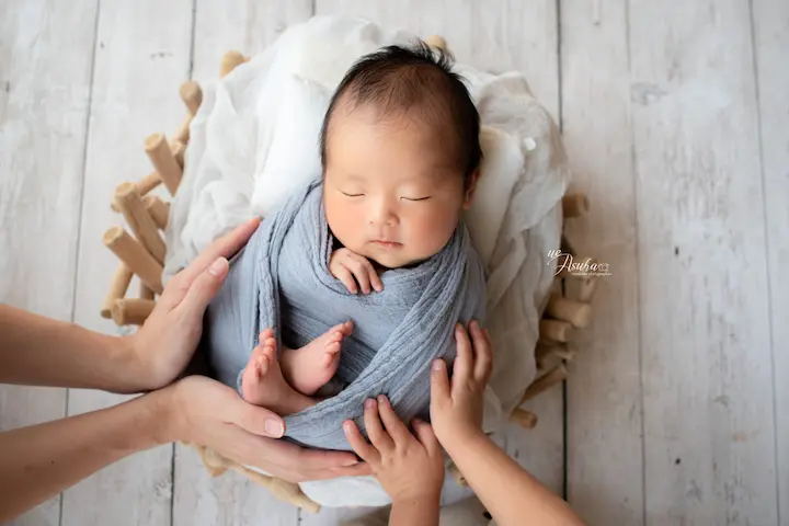 ニューボーンフォト灰色の布に包まれたバスケットの赤ちゃん