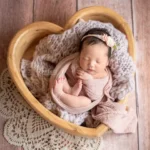 ニューボーンフォト_花のヘッドバンドとピーチ色のおくるみに包まれたハートボウルの新生児