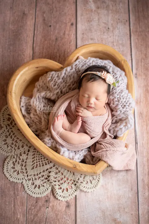 ニューボーンフォト_花のヘッドバンドとピーチ色のおくるみに包まれたハートボウルの新生児
