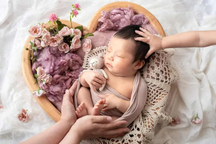 ニューボーンフォト_きょうだいに頭をなでられる花冠の赤ちゃんとハートバスケット