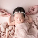 ニューボーンフォト_ピンクの布に包まれ、両親と手をつなぐ新生児