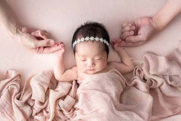 ニューボーンフォト_ピンクの布に包まれ、両親と手をつなぐ新生児